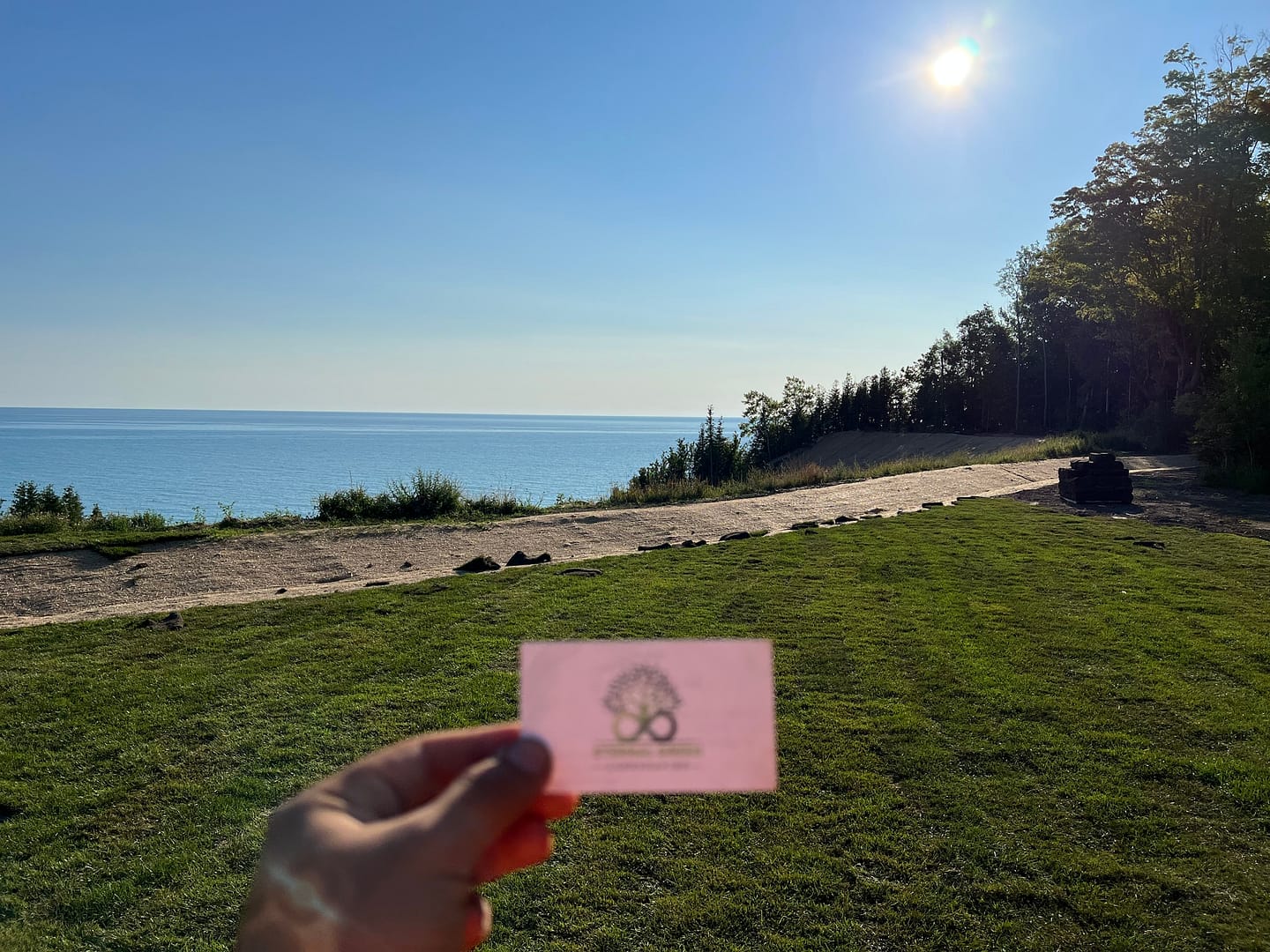 Person holding a business card with a scenic lakefront landscape in the background.