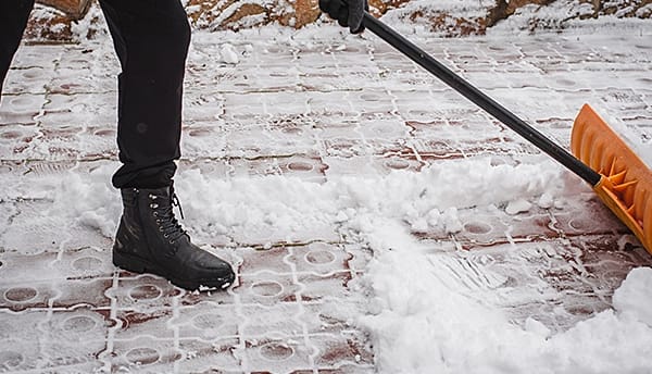 Person clearing snow from a walkway with a push shovel.