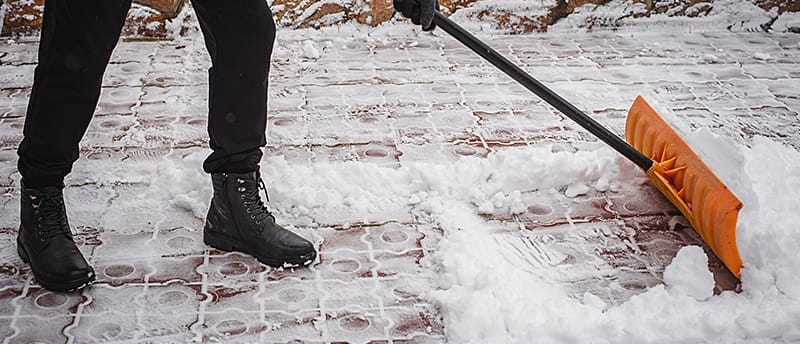 Person clearing snow from a walkway with a push shovel.